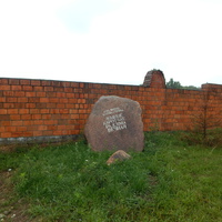 У ограды костела мемориальный камень с текстом о жизни и родине.