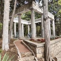 Античная беседка в парке на территории дворца Харакс из 12 мраморных колонн на невысоком стилобате, выполненных в «римском ордере помпейского типа». По одной из версий, это были подлинные  античные элементы, но при послевоенном ремонте были утрачены.