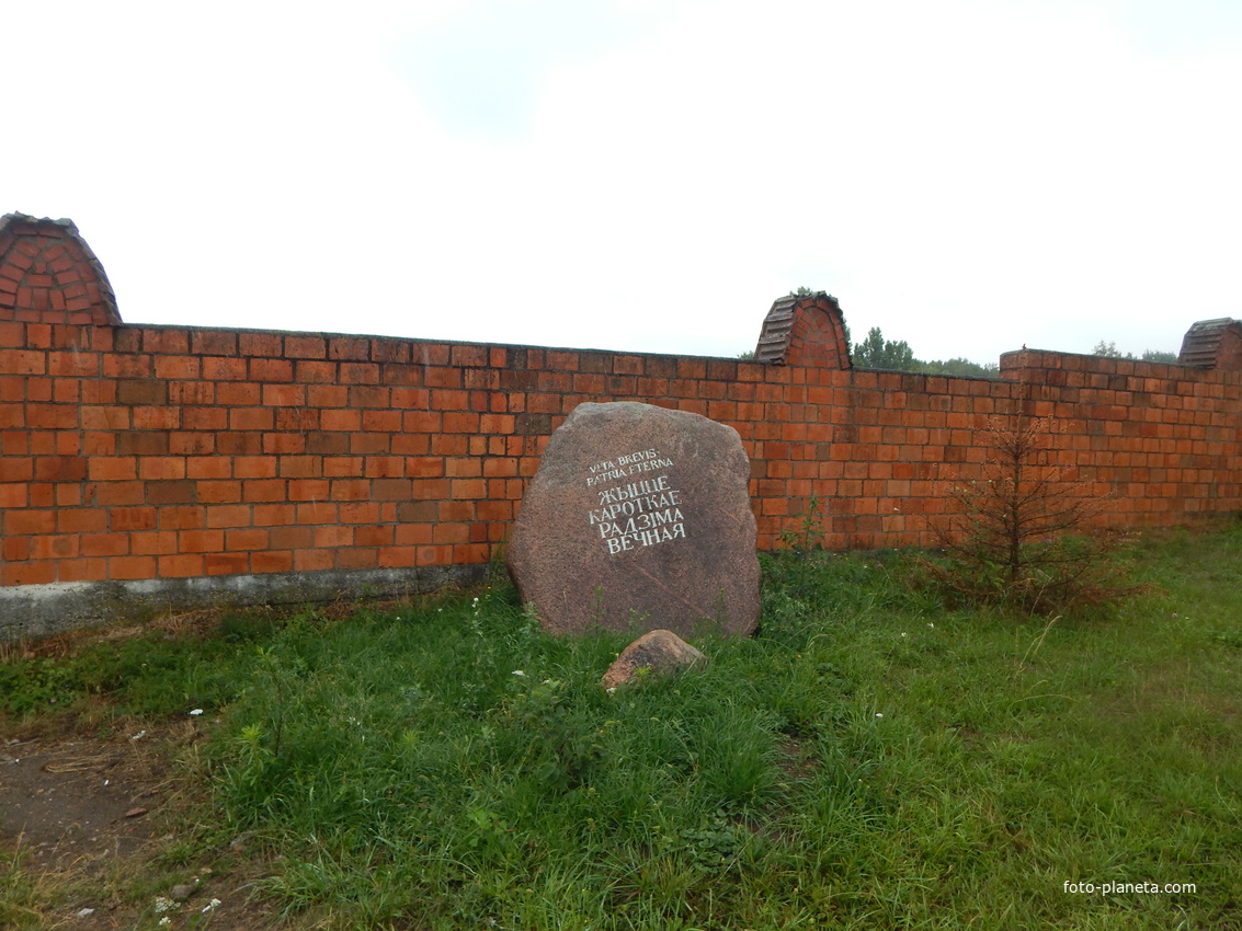 У ограды костела мемориальный камень с текстом о жизни и родине.
