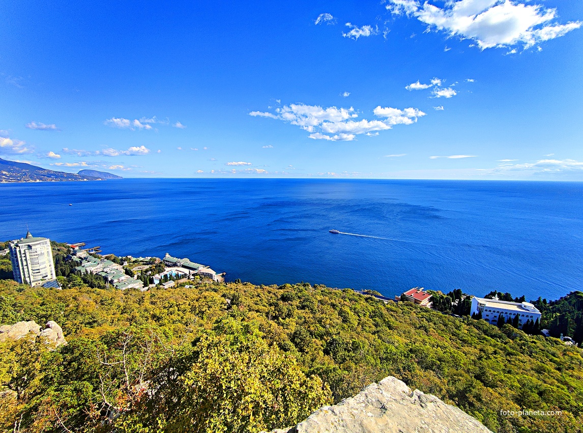 Вид на Черноморское побережье со скалы Утюг. Справа - территория санатория "Кичкине" ФСО РФ (закрытая) в п.г.т. Гаспра с дворцом Кичкине (летняя резиденция князя Д. К. Романова). Слева - строения отеля Пальмира Палас и высотный ЖК "Южная Пальмира".