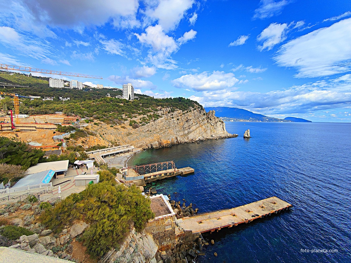 Вид со смотровой площадки замкового комплекса "Ласточкино гнездо" на вершине Аврориной скалы на побережье мыса Ай-Тодор с действующей и строящейся инфраструктурой и его восточный (Лимен-Бурун) отрог с отдельной маленькой скалой Парус.