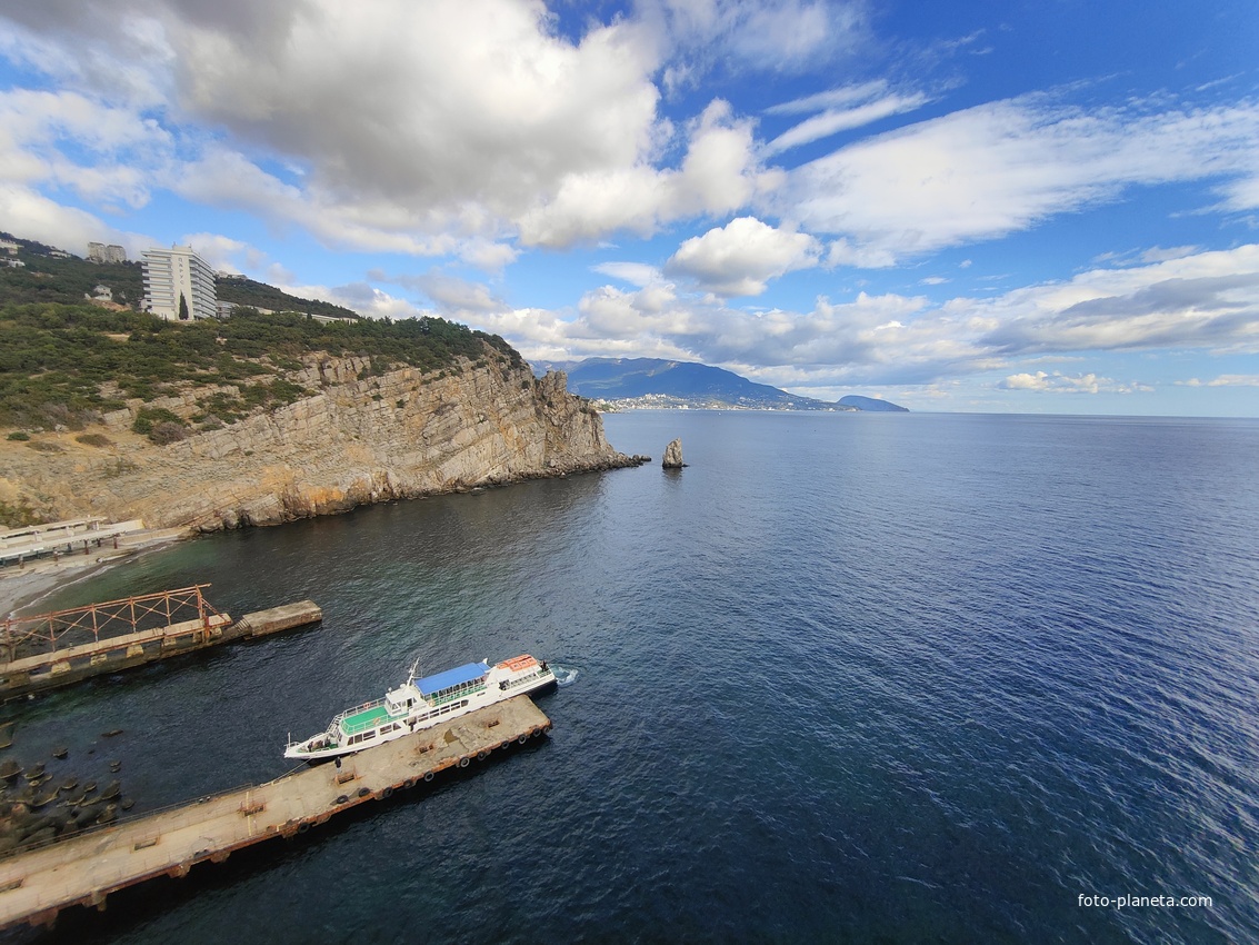 Вид со смотровой площадки с балюстрадой у западной стены замка "Ласточкино гнездо" на вершине Аврориной скалы на окружающую акваторию и восточный (Лимен-Бурун) отрог с отдельной маленькой скалой Парус мыса Ай-Тодор.