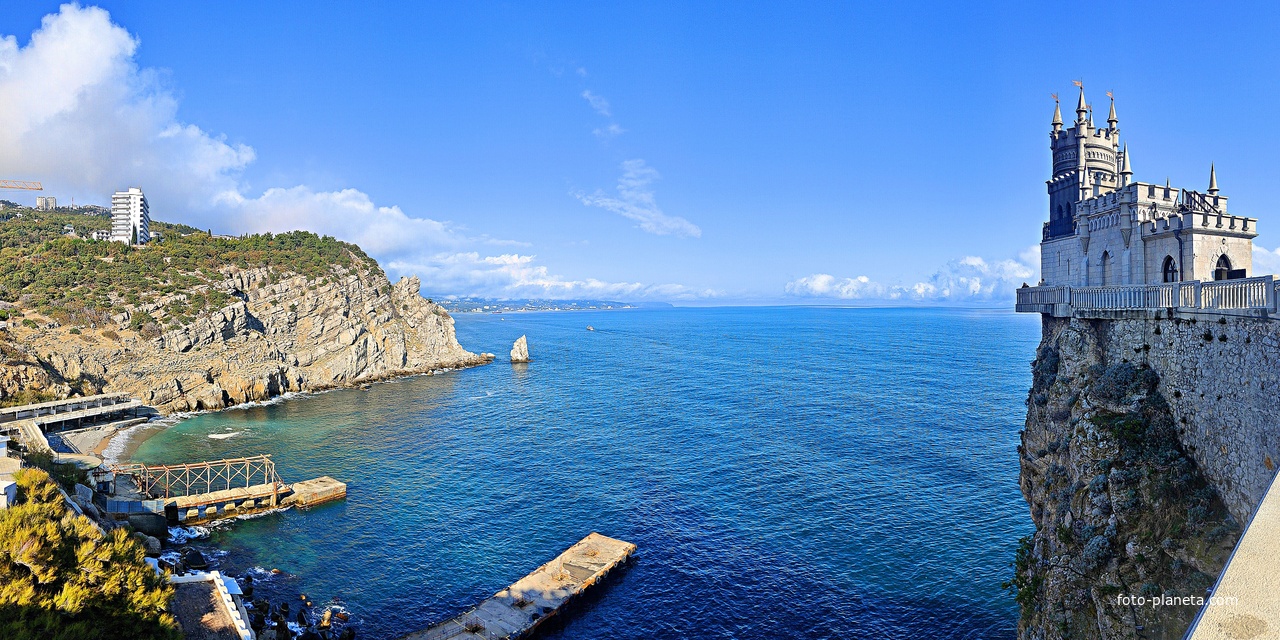 Вид со смотровой площадки во внутреннем дворе замкового комплекса "Ласточкино гнездо" на вершине Аврориной скалы на псевдоготический замок, окружающую акваторию, побережье и восточный (Лимен-Бурун) выступ мыса Ай-Тодор с маленькой скалой Парус.