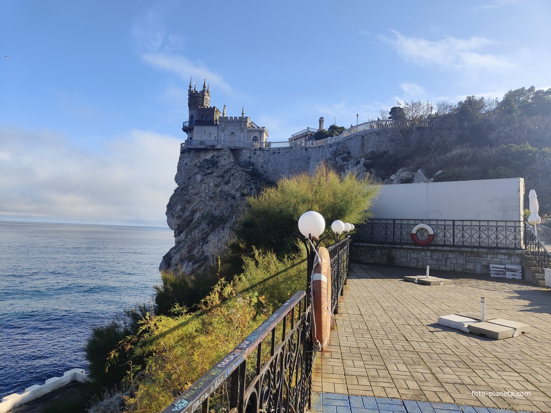 Вид с площадки на склоне Аврориной скалы (среднего отрога Монастыр-Бурун) мыса Ай-Тодор на псевдоготический замок "Ласточкино гнездо" и балюстраду смотровой площадки внутреннего двора замкового комплекса.