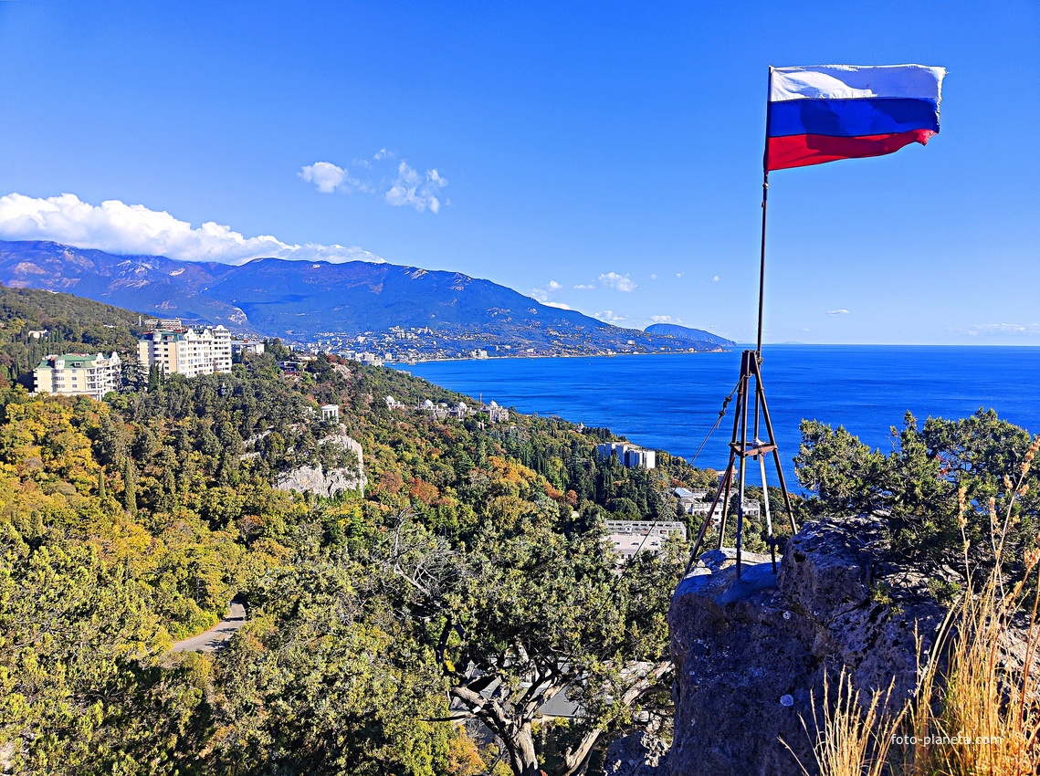 На вершине горы Урьянда (Крестовая). Флаг РФ, установленный в 2014г. Вид на акваторию, побережье с застройкой посёлка Ореанда. В центре - полуротонда на Царской тропе. Далее - застройка Ливадии и Ялты на южном склоне Главной гряды Крымских гор.