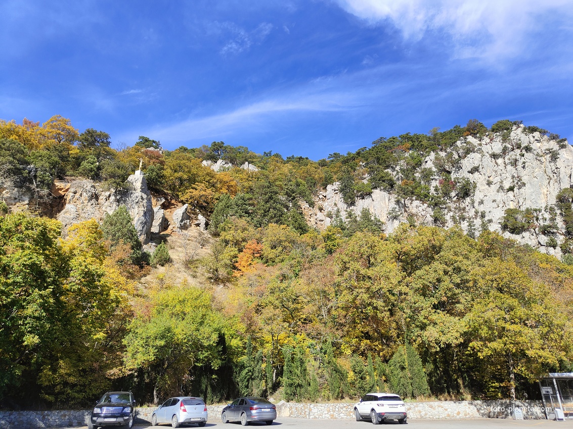 Автостоянка перед храмовым комплексом Архистратига Божия Михаила на Севастопольском шоссе над посёлком Ореанда. Выше - ребро склона горы Ай-Никола с Крестом и Распятием на навершие выступа скалы.