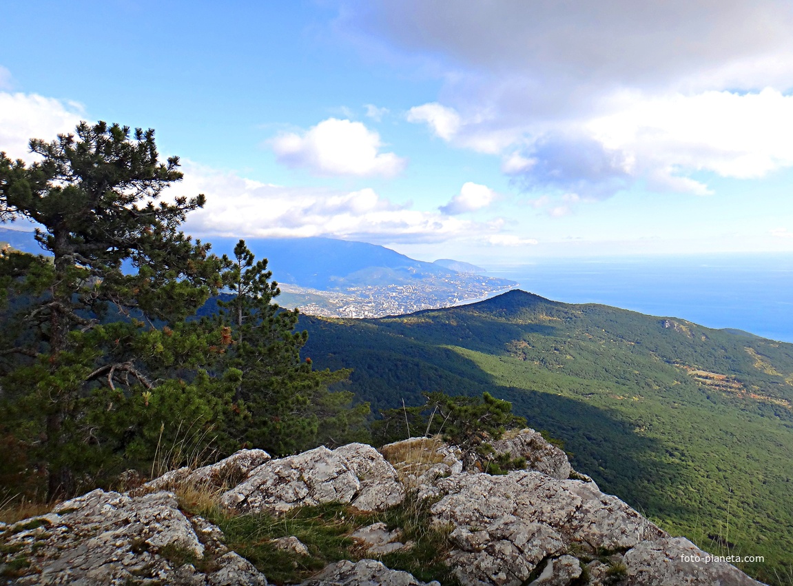Вид с Кореизской тропы в Ялтинском горно-лесном заповеднике на обрыве перед вершиной Ай-Петринской яйлы на побережье и акваторию Чёрного моря, в центре - зелёный конус г. Могаби, за ним - жилая застройка Ялты.